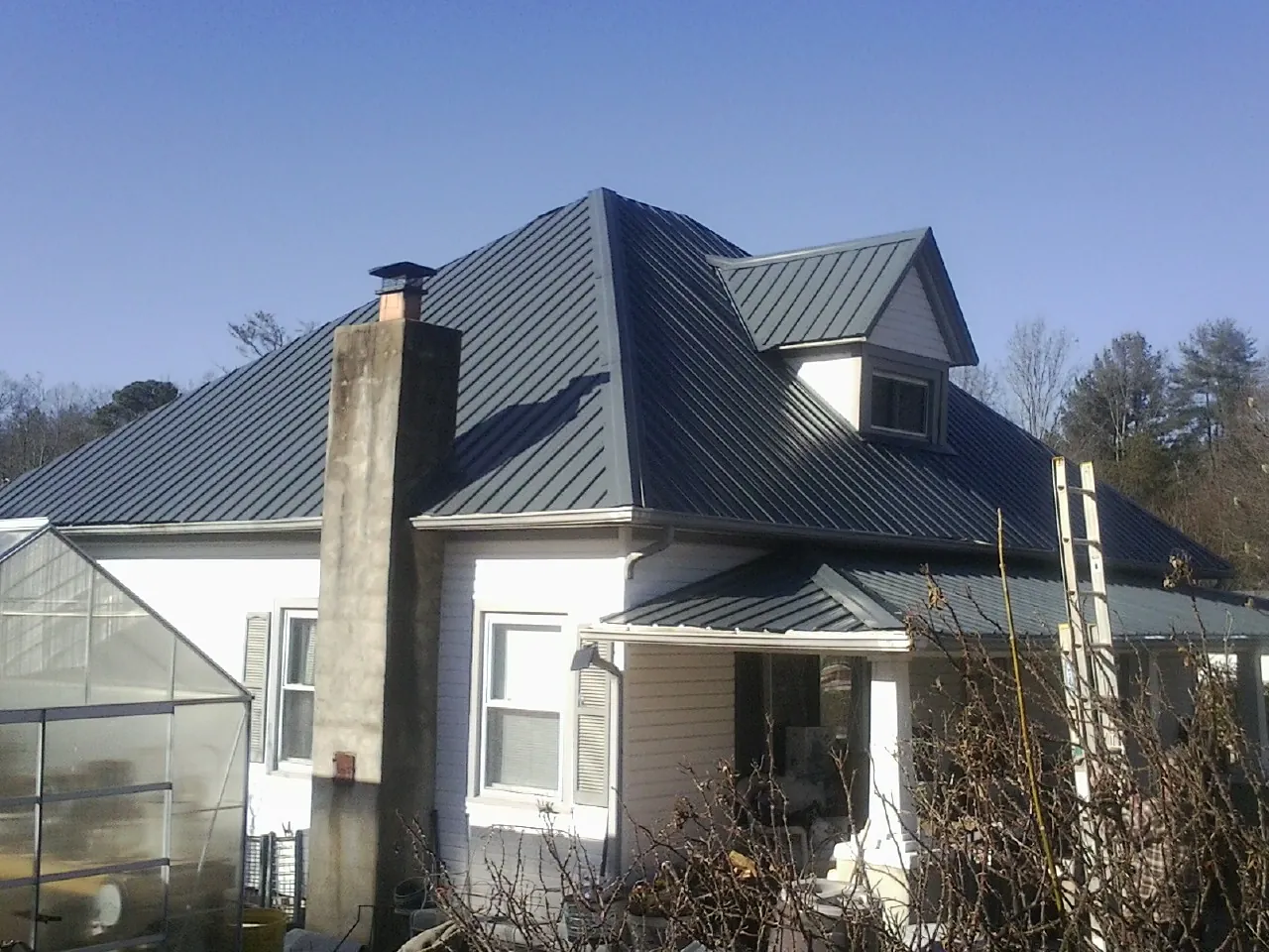 Dark blue standing seam metal roof on a white farmhouse with dormer — Slate & Tile Roof Repair by Roofing Brothers in Chimney Rock