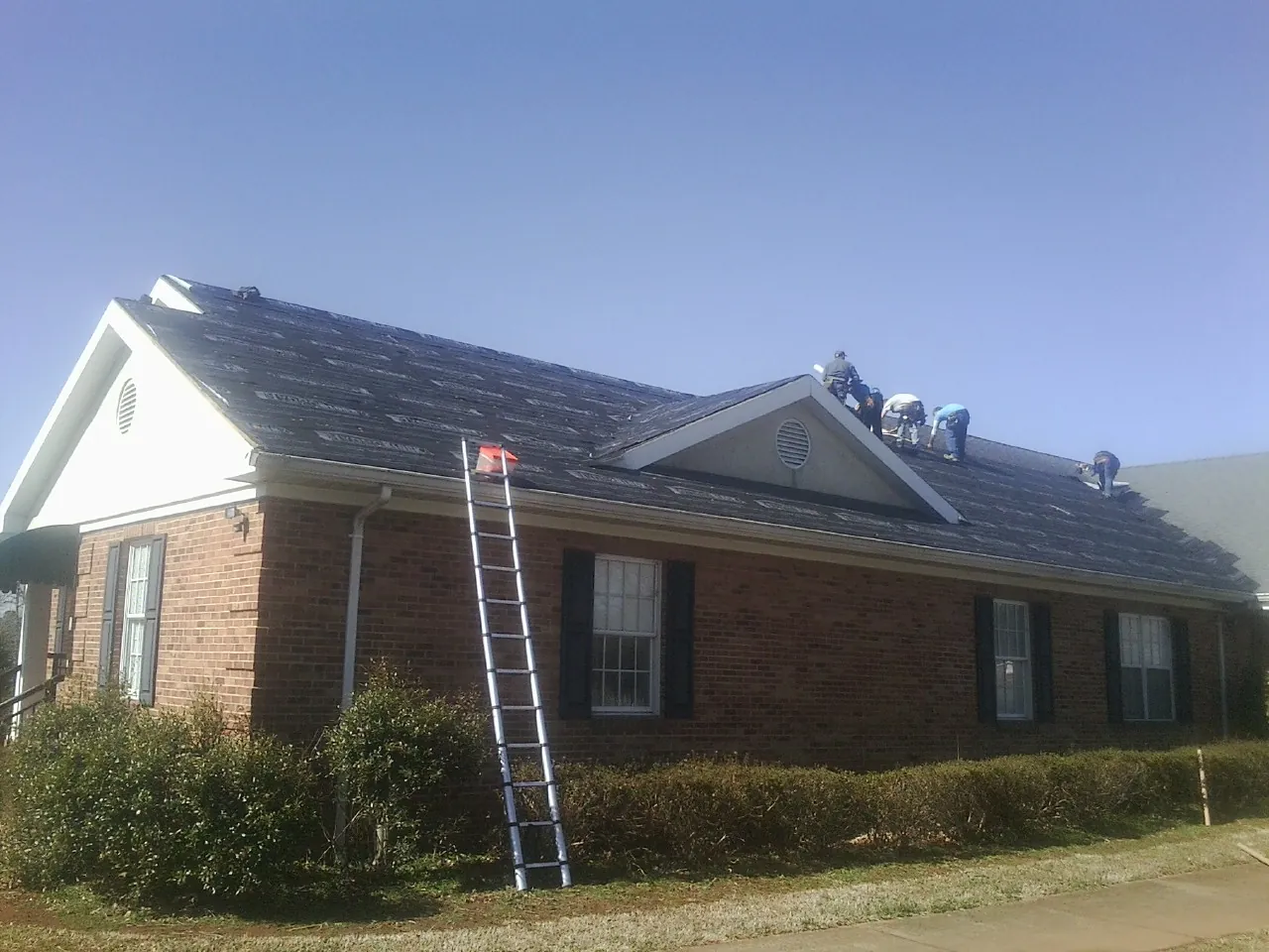 Crew tearing shingles off a brick ranch roof with a ladder set — Metal Roof Repair work by our crew in Chimney Rock
