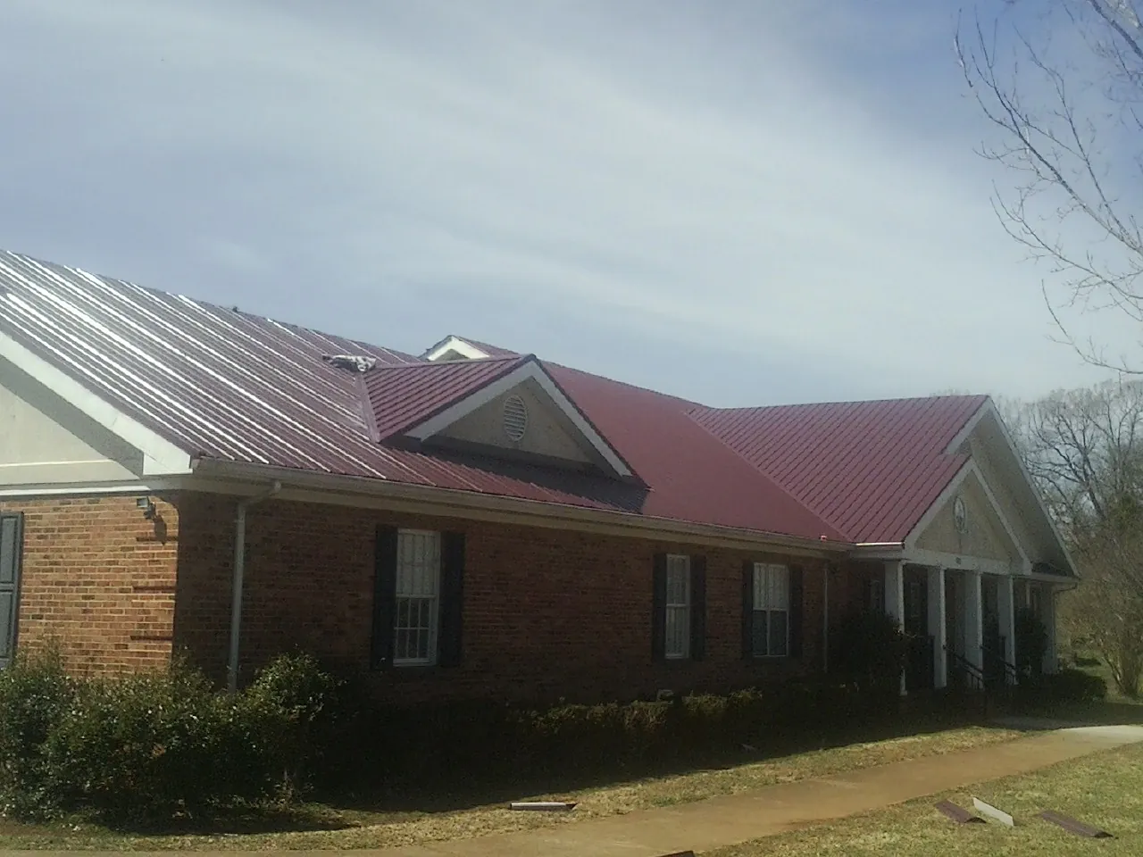 Red metal roof with gabled entries on a long brick building, from a Hail Damage Roof Repair job in Chimney Rock