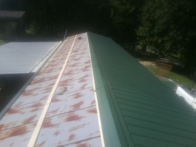 Old rusted panels beside newly installed green metal roofing — Wind Damage Roof Repair by Roofing Brothers in Chimney Rock