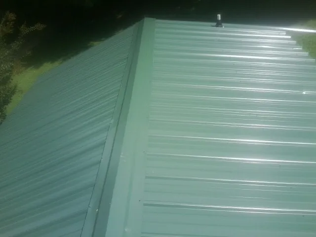 New green metal panels meeting at the ridge of a roof — Flat Roof Repair work by our crew in Chimney Rock