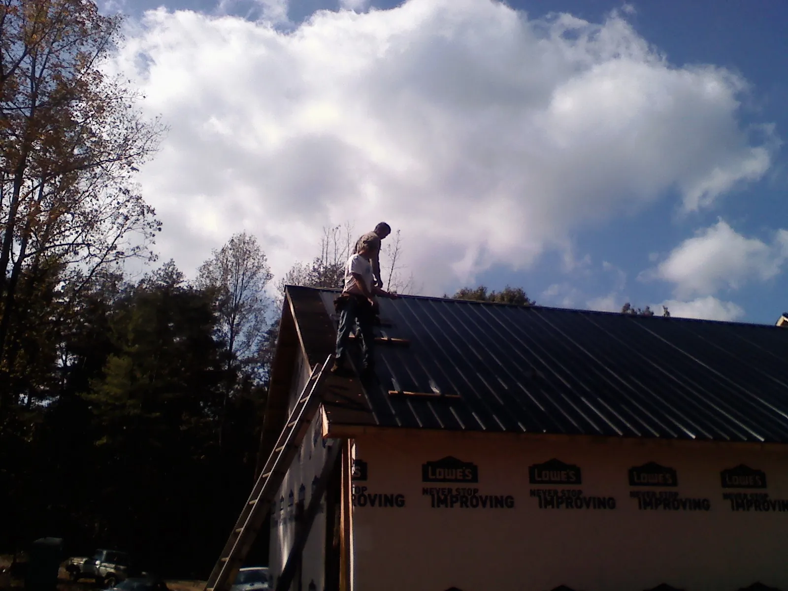 Roofer fastening dark metal panels high against a cloudy sky, from a Roof Inspection job in Chimney Rock