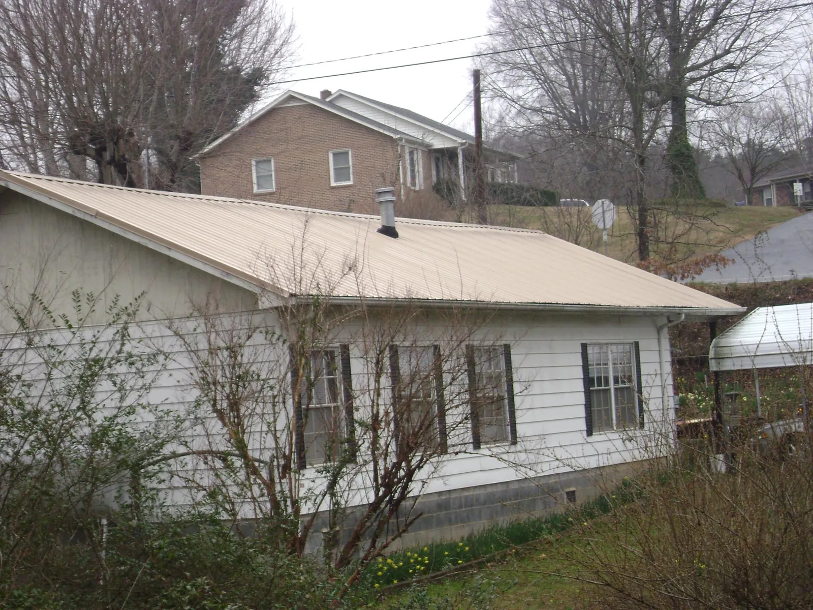 Tan metal roof on a white sided house set into a hillside — Commercial Roofing by Roofing Brothers in Chimney Rock