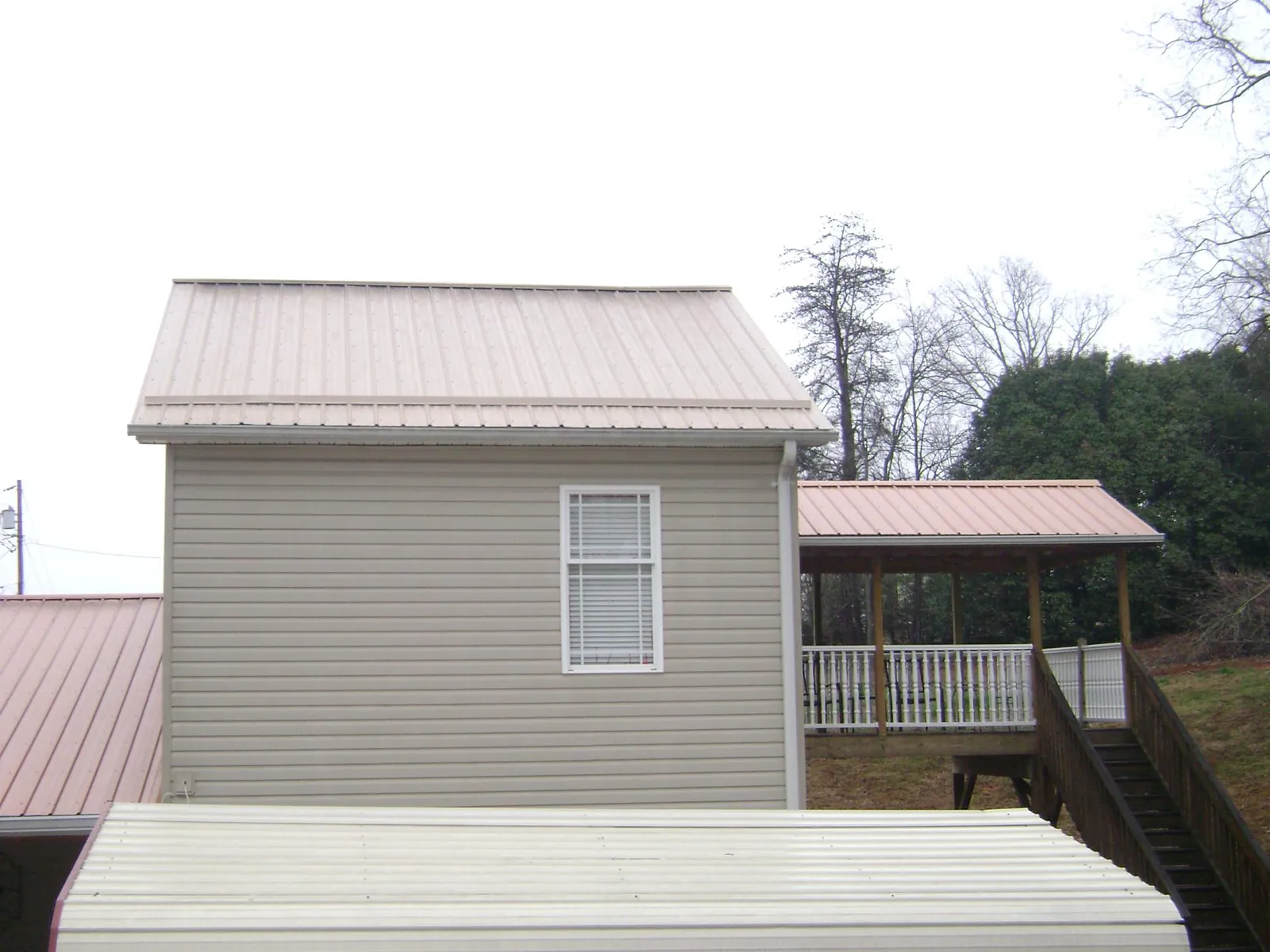 Tan metal roofs on a two story addition and attached porch, from a Roof Replacement job in Chimney Rock